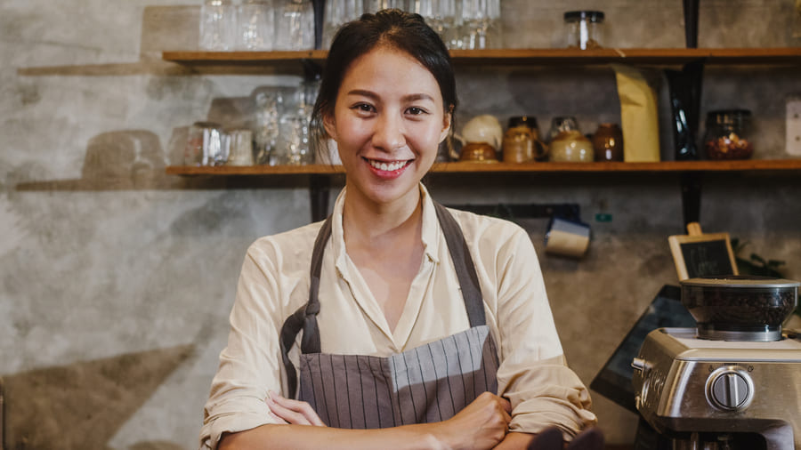 Mulher asiática sorrindo com os braços cruzados em um café.